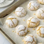 Freshly baked lemon crinkle summer cookies coated in powdered sugar on a baking tray.