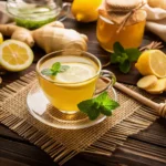 Glass cup of ginger lemon honey tea with lemon slice and mint garnish, surrounded by fresh ginger, lemons, honey jar, and a honey dipper on a wooden table — a natural and soothing drink idea from Zepbound Recipes.