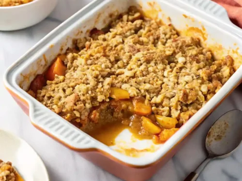 Top-down view of warm peach crisp in a white baking dish, one scoop missing to reveal the juicy filling—Mom’s classic recipe.