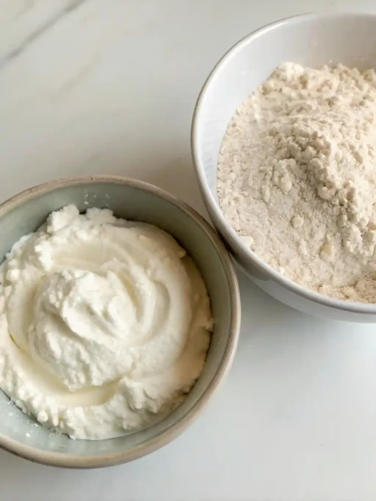 Bowls of plain Greek yogurt and self-rising flour, the only ingredients needed to make 2 ingredient Greek yogurt biscuits.