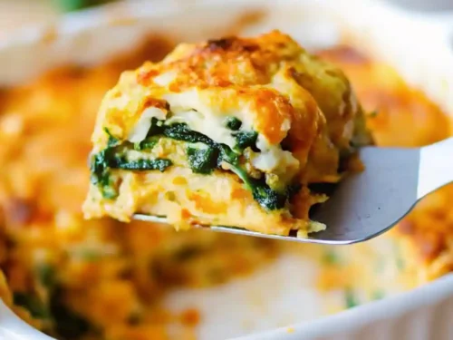 a slice of butternut squash and spinach lasagna lifted out of a white casserole dish