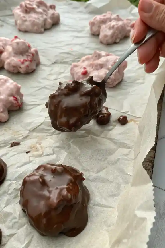 Placing homemade chocolate-coated yogurt and strawberry bites on a baking tray to set.