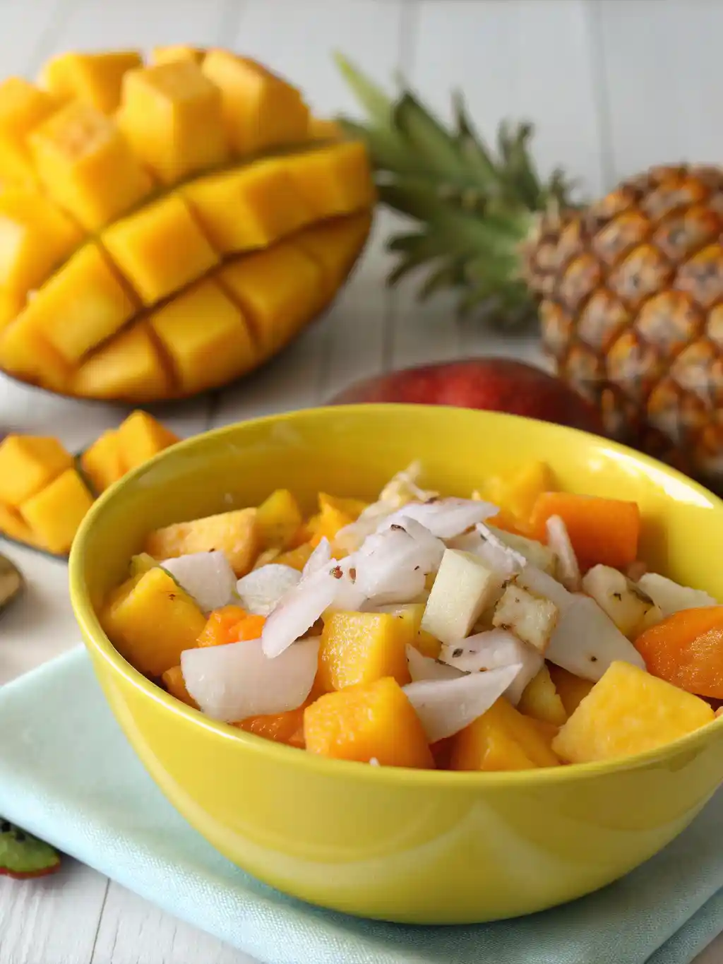 Tropical fruit salad in a yellow bowl with mango, pineapple, coconut, and papaya chunks