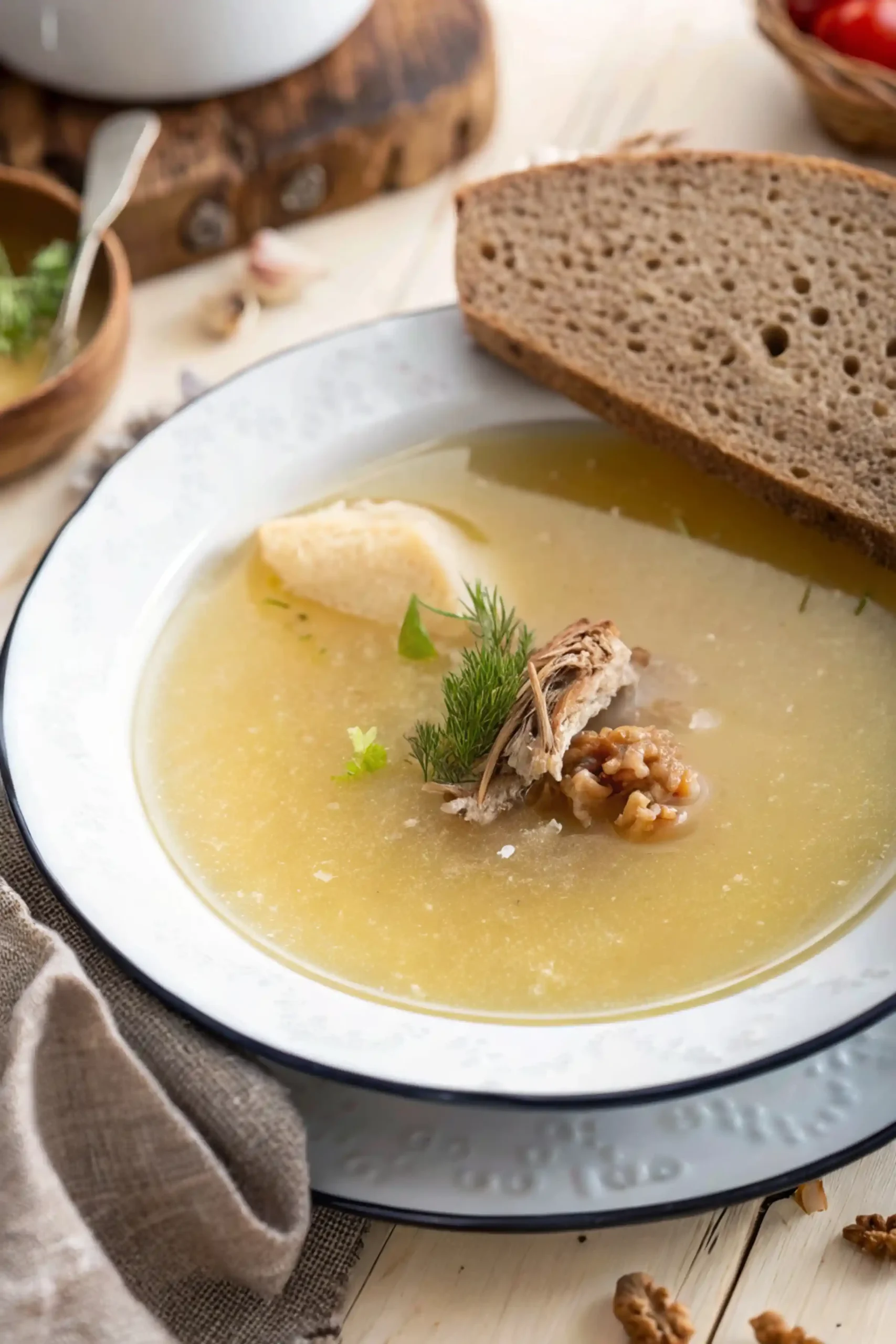 Homemade Jewish chicken soup recipe with dill and shredded chicken, served alongside a slice of brown bread on a white plate with a blue rim.